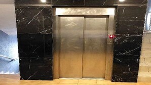 An elevator with a metallic finish, flanked by black marble walls, and a red emergency button on the right side. - Hotel Meumi Palace (Yaoundé)