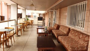 A cafe with wooden tables and chairs, a sofa, and a tiled floor. - Hotel Meumi Palace (Yaoundé)