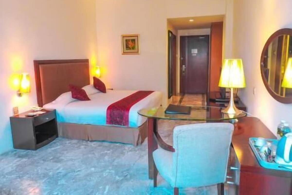 A hotel room with a bed, bedside lamps, a desk with a chair, and a mirror.