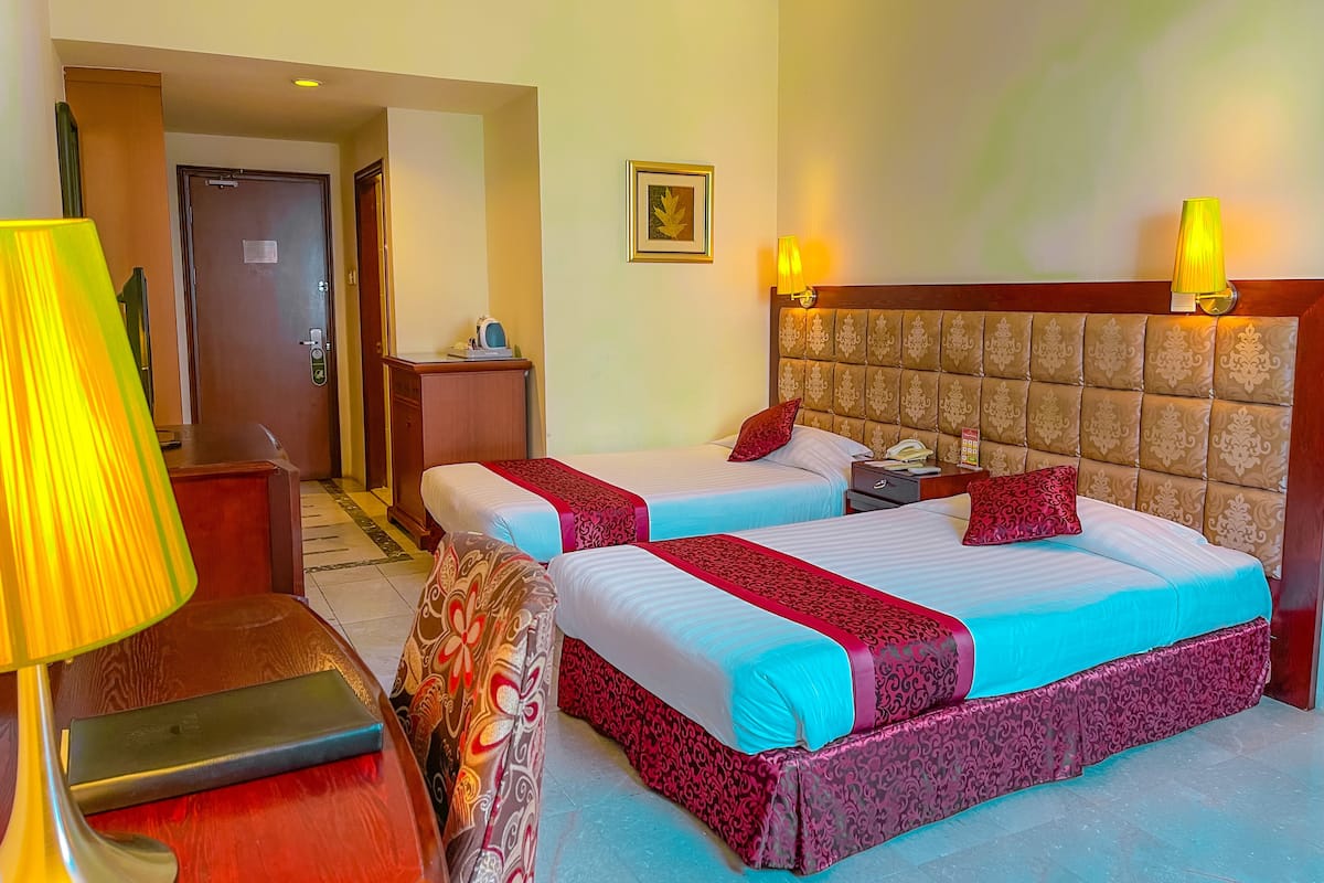 A hotel room with two beds, a bedside table, a lamp, and a door.