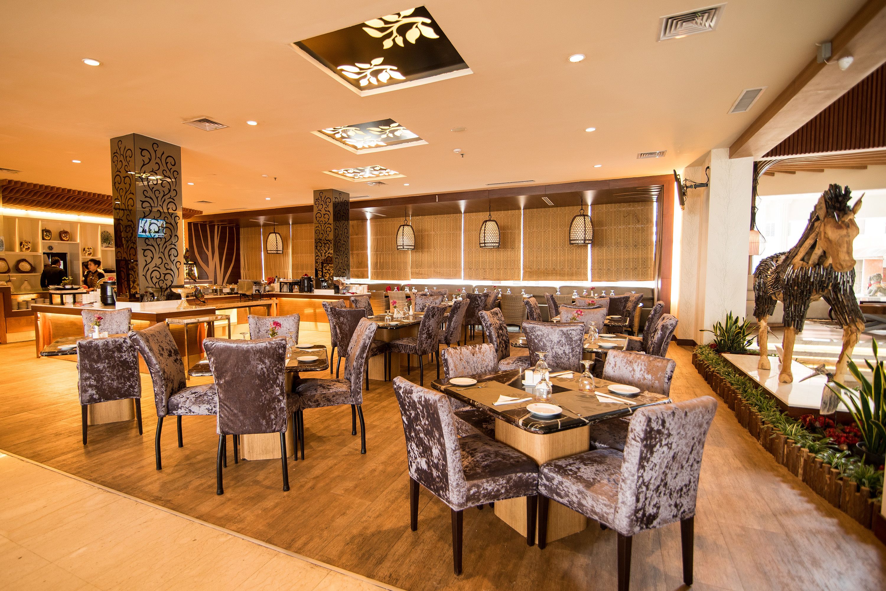 Un amplio vestíbulo de hotel con una zona de bar central, varios conjuntos de asientos y elementos decorativos como una escultura de jirafa y luces fijadas a la pared.