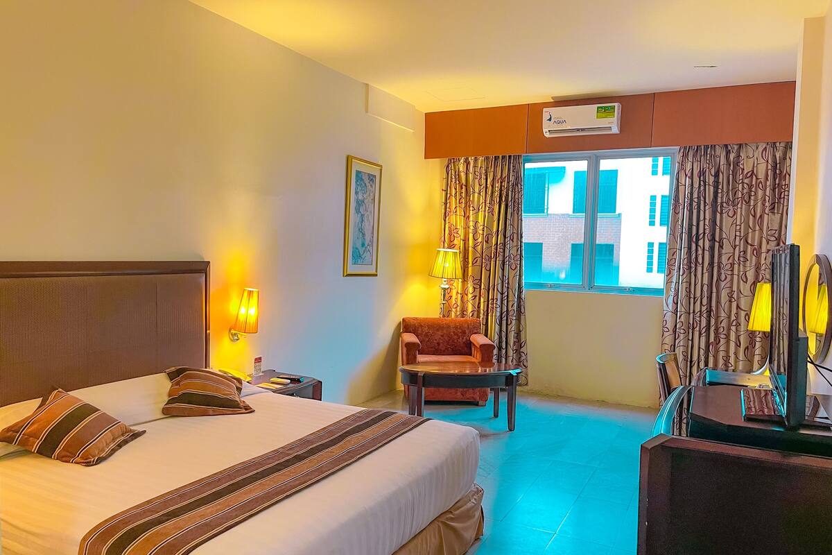 A hotel room with a bed, a chair, a desk with a mirror, and a window with curtains.