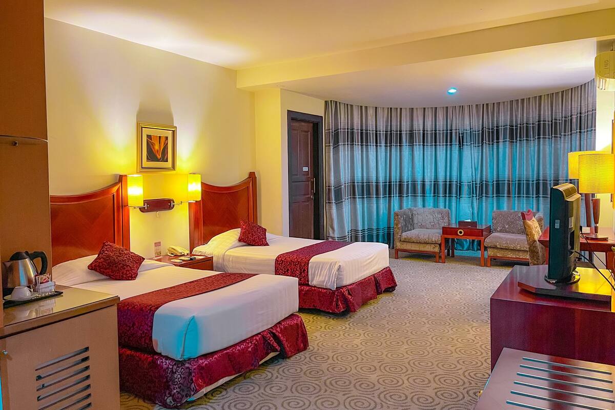 A hotel room with two beds, a desk, a chair, and a television.