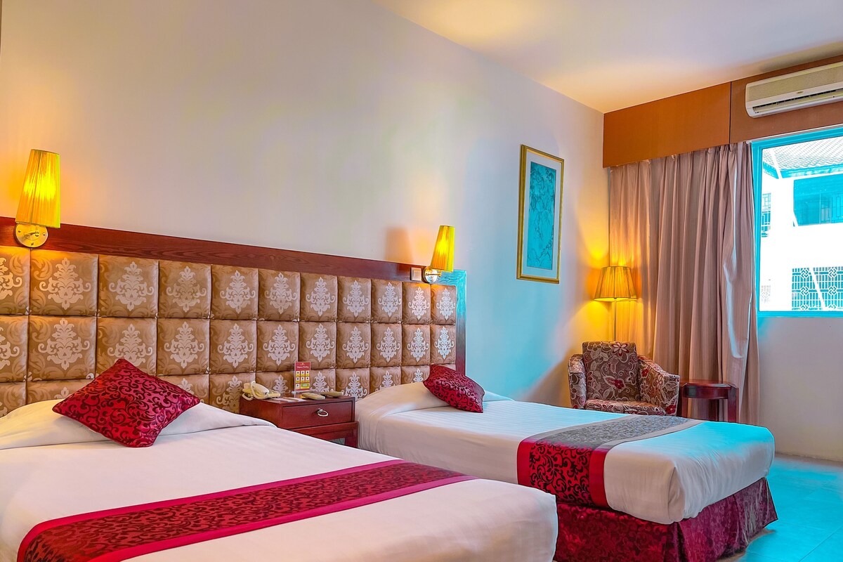 A hotel room with two beds, a headboard, bedside lamps, a nightstand, a chair, and a window with curtains.