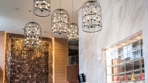 Un vestíbulo moderno con mostrador de recepción de mármol, pared de piedra y candelabros de cristal colgantes.