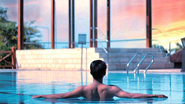 Un hombre en una piscina con una estructura de madera al fondo.