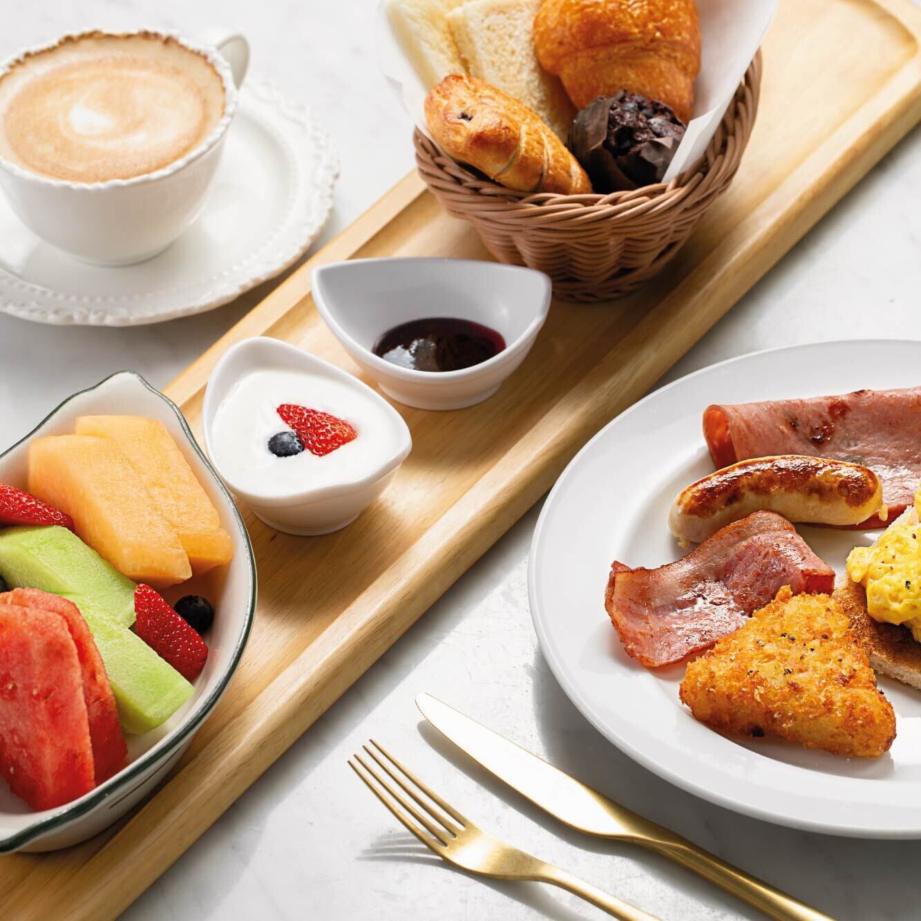 A breakfast tray with croissants, ham, sausages, fried eggs, and fruit.