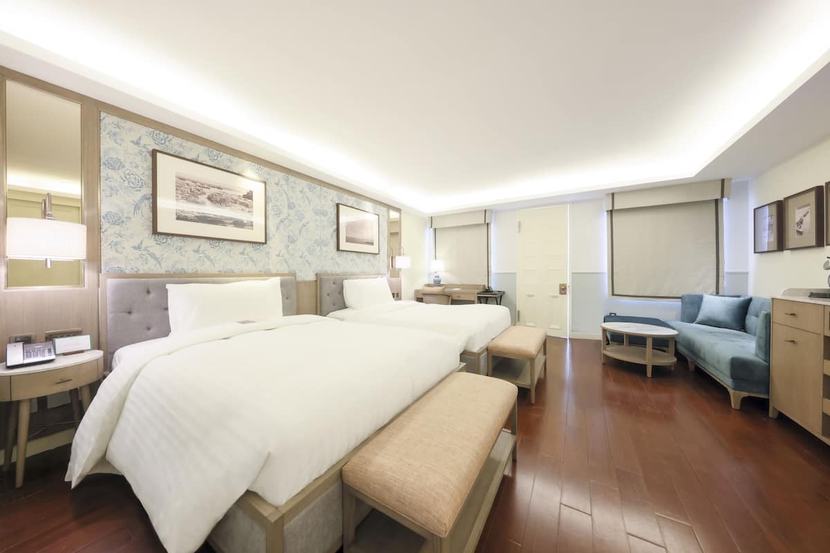 Een hotelkamer met drie bedden, een bank, een klein tafeltje en een bureau met een lamp.