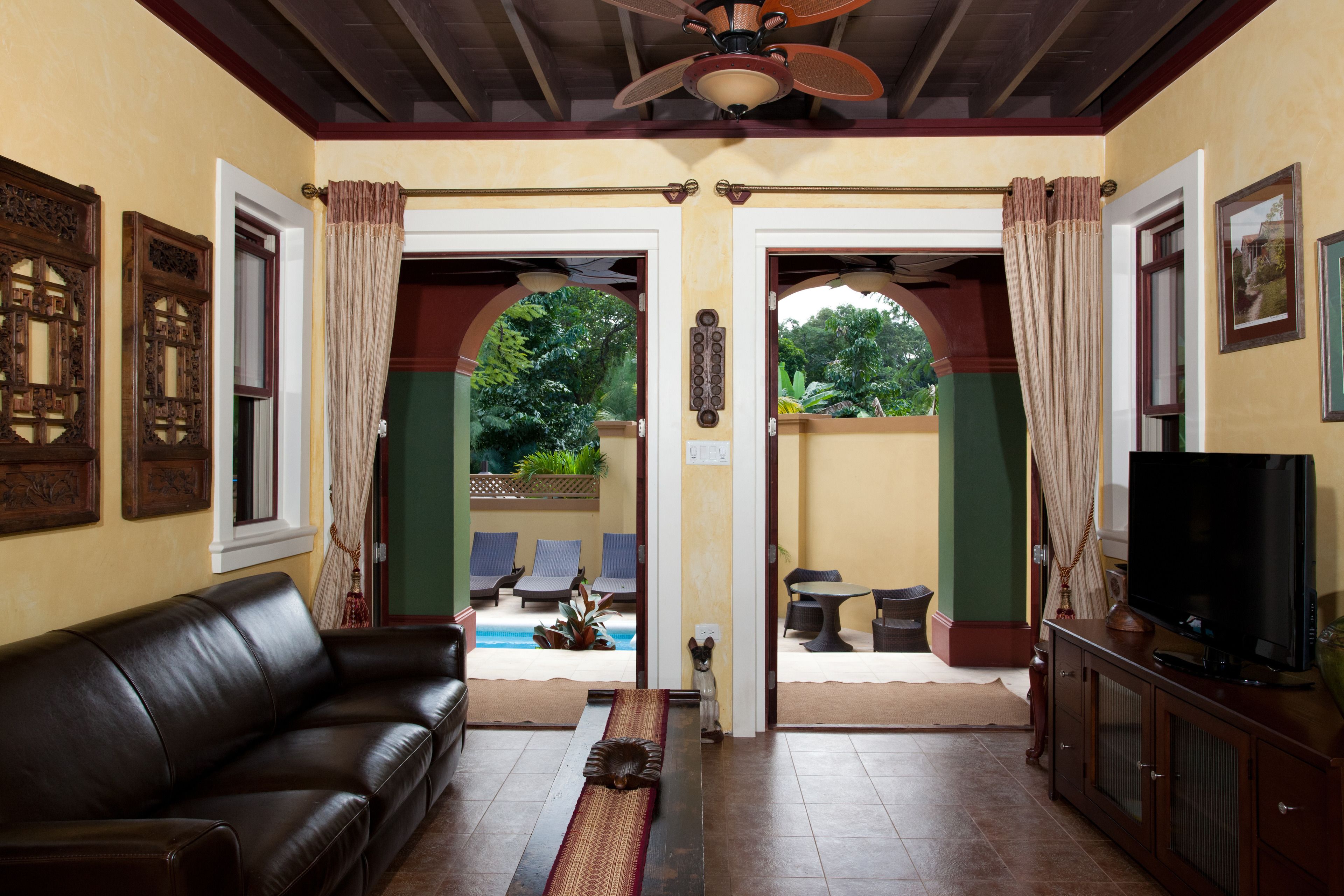A living room with a leather sofa, a television, and a view of an outdoor pool area.