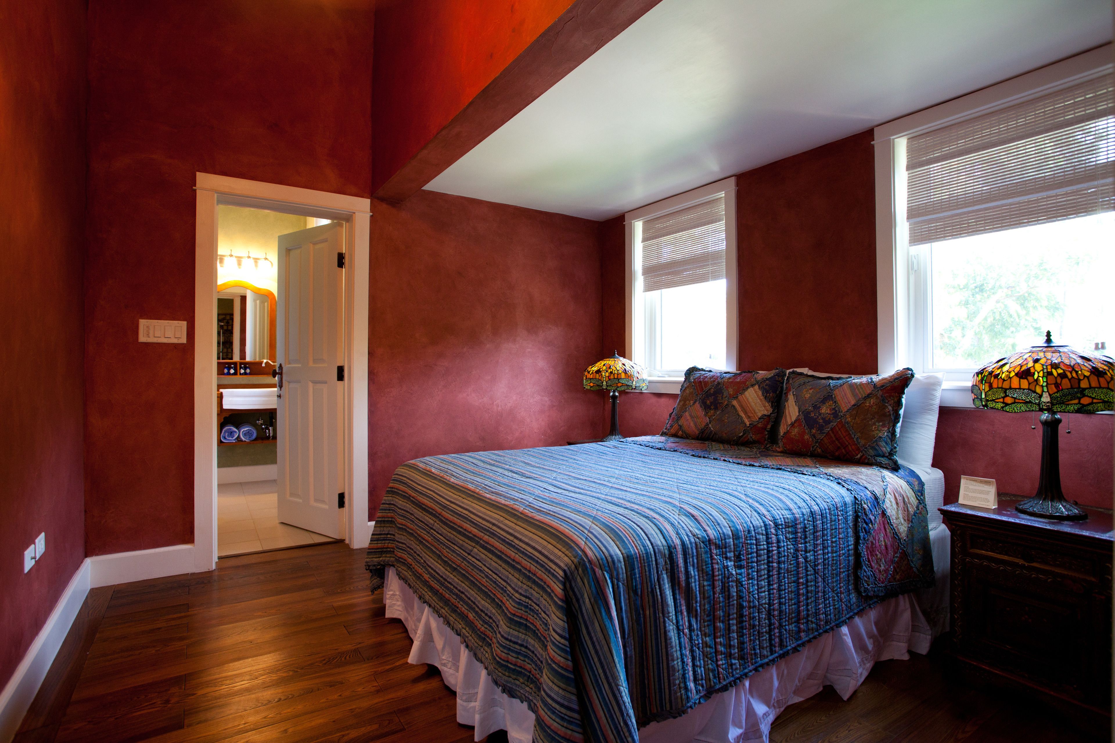 A bedroom with a large bed, a nightstand, a lamp, and a window with blinds.
