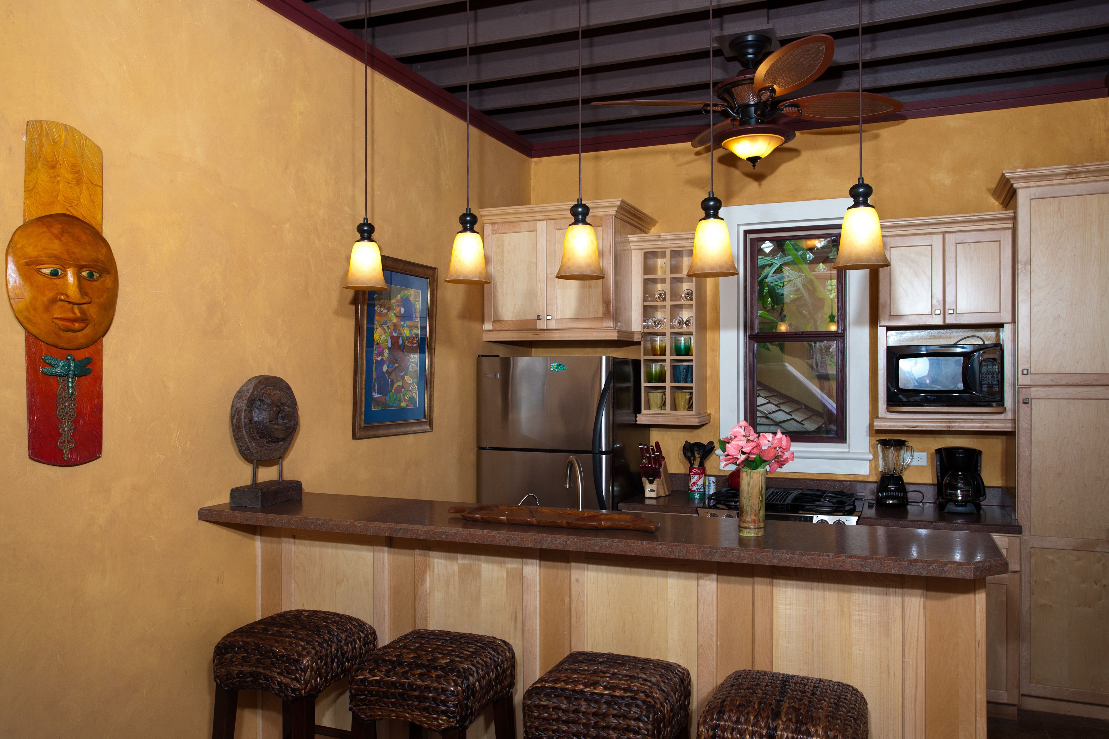 A kitchen with wooden cabinets, a stainless steel refrigerator, a microwave, and a bar area with stools.