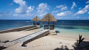 Ein Strand mit zwei strohgedeckten Hütten und einem Steinweg, der zum Wasser führt.