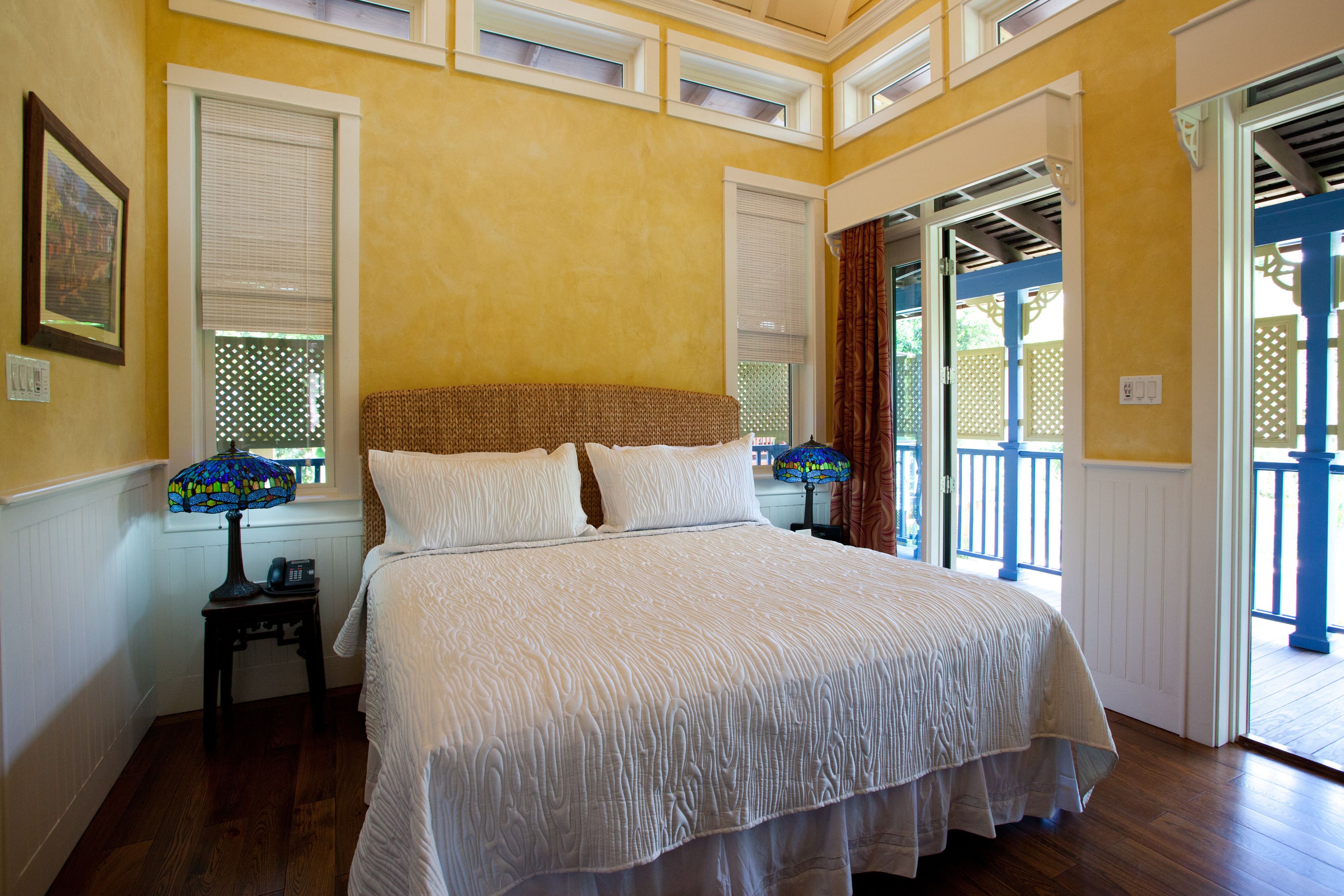 A bedroom with a large bed, a nightstand with a lamp, and a window with blinds.
