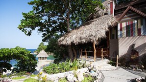 Ein tropisches Resort mit einer strohgedeckten Struktur, Blick auf den Strand und einer kleinen Hütte.