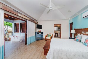 Ein Schlafzimmer mit einem großen Bett, einem Deckenventilator, einem Fernseher, einer hölzernen Kommode und einem Badezimmer mit Badewanne und Dusche.