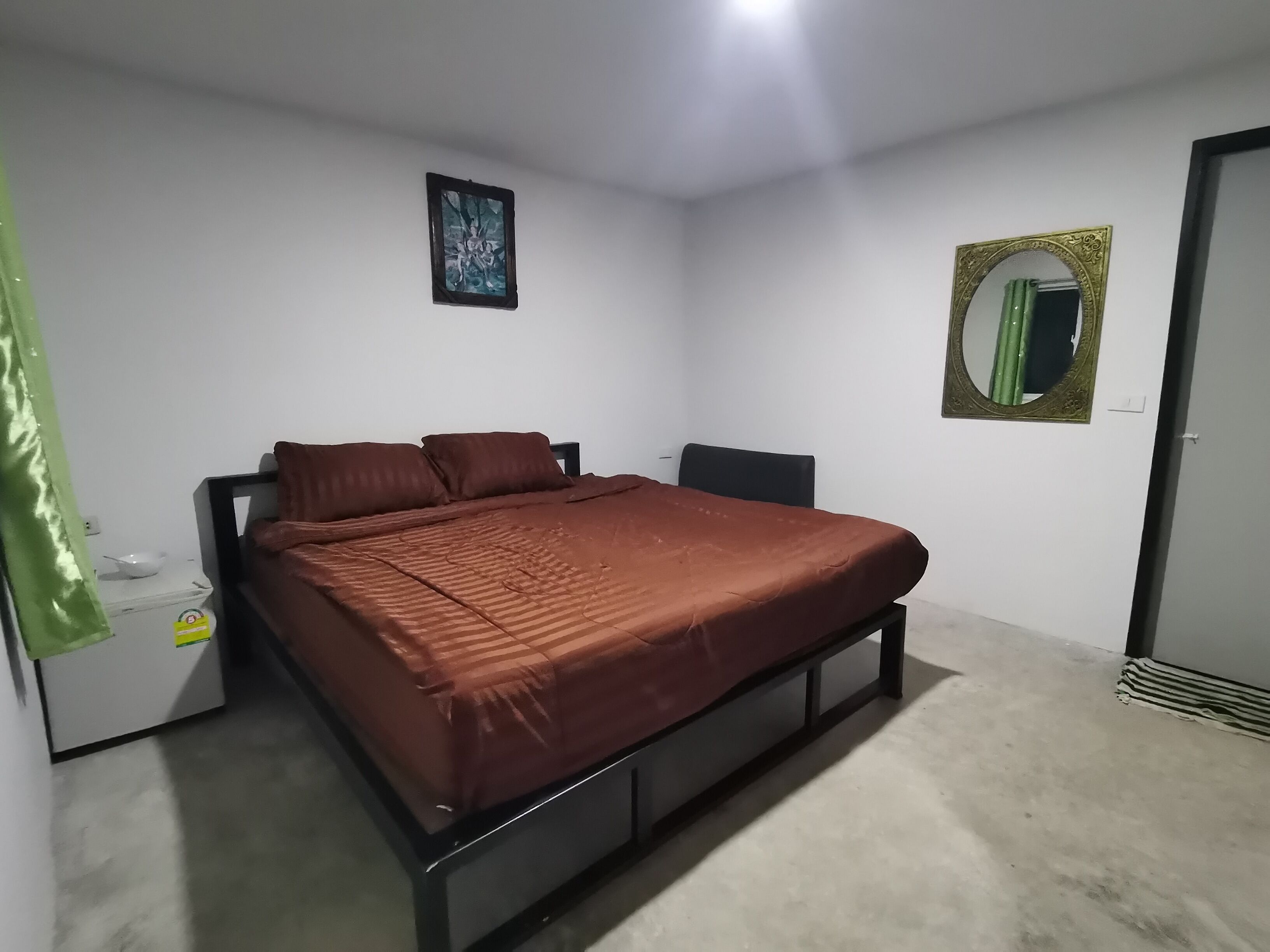 A bedroom with a bed, a wall-mounted mirror, and a framed picture.