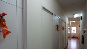 A corridor with white walls, a tiled floor, and a door at the end. - Grace Naha - Hostel (Naha)