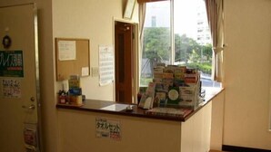 A reception desk with a window view, a bulletin board, and a sign indicating a room rate. - Grace Naha - Hostel (Naha)