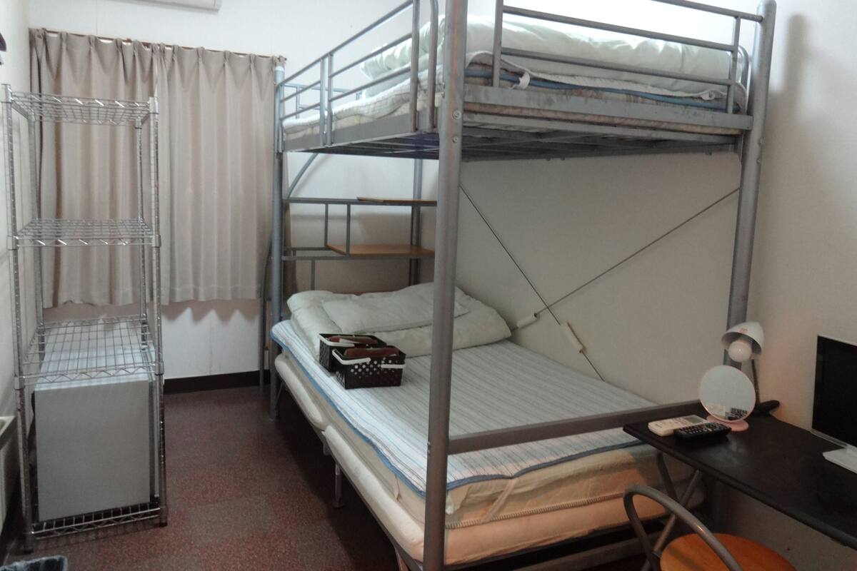 A bunk bed room with a metal shelf unit, a desk with a mirror, and a chair.