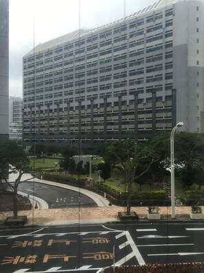 Un edificio moderno con fachada de estructura cuadriculada, rodeado de un área ajardinada con árboles y una carretera curva.