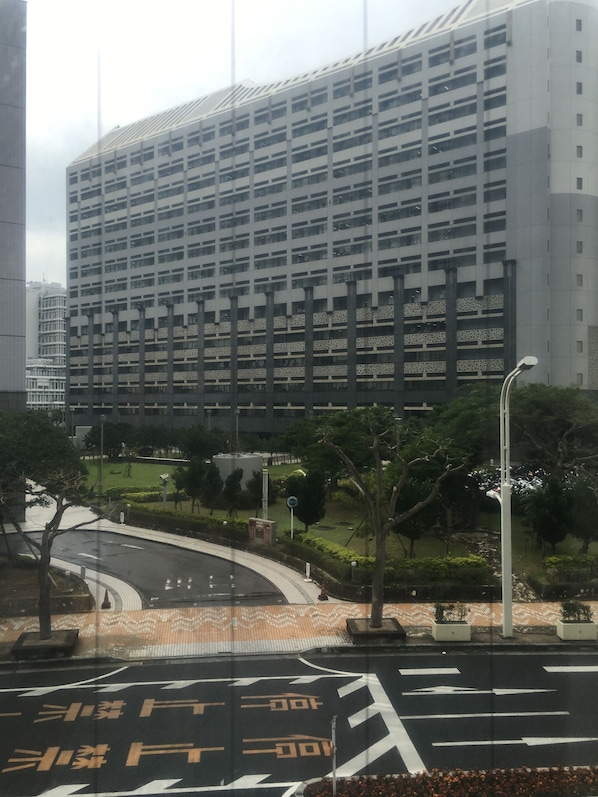 Un edificio moderno con fachada de estructura cuadriculada, rodeado de un área ajardinada con árboles y una carretera curva.