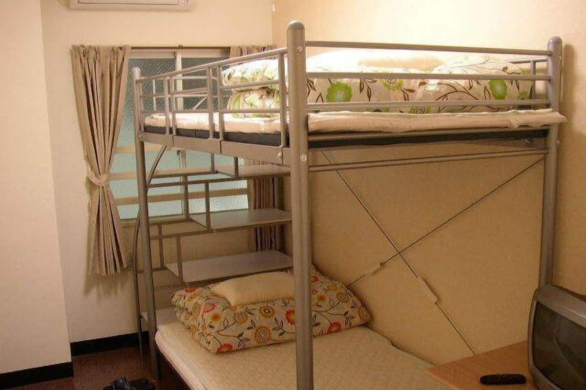 A bunk bed with a television on a wooden table, a window with curtains, and a pair of shoes on the floor.