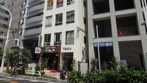 A multi-story building with a restaurant on the ground floor, a parking garage on the right, and a sign for a dental clinic on the left. - Grace Naha - Hostel (Naha)
