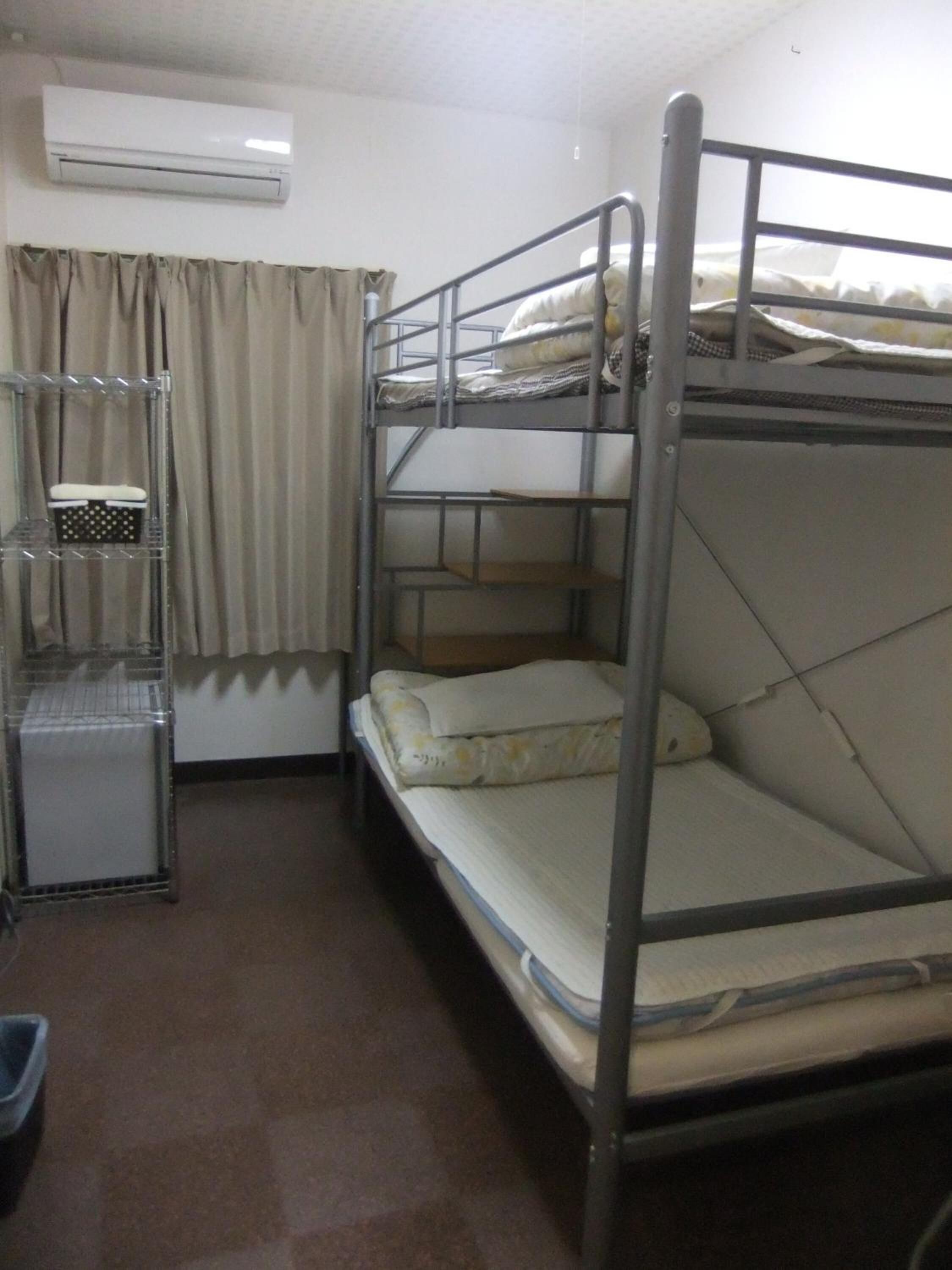 A bunk bed room with a metal frame, a small desk with a chair, and an air conditioning unit on the wall.