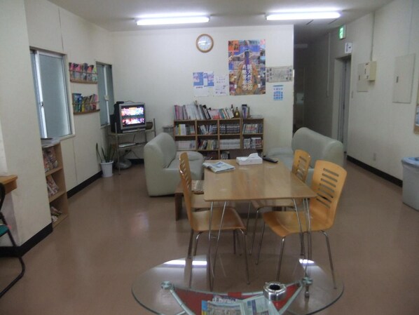 Un salón de conferencias con una mesa de vidrio, cuatro sillas, una estantería, un televisor y un reloj en la pared.
