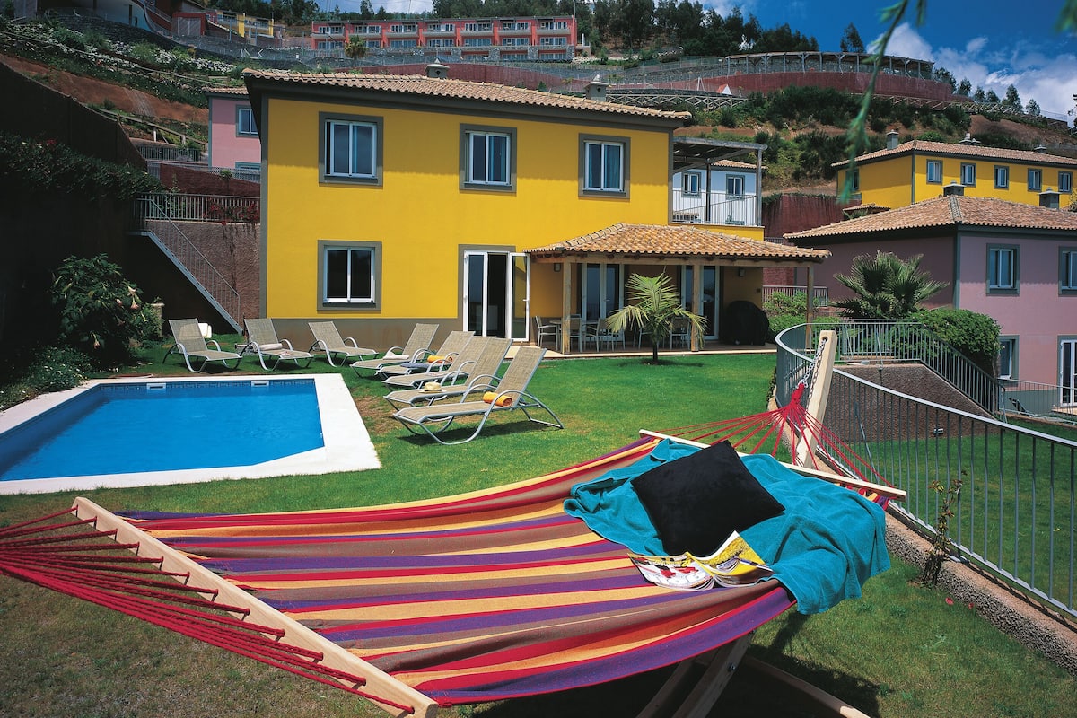 A residential area with a swimming pool, a hammock, and a view of colorful houses.
