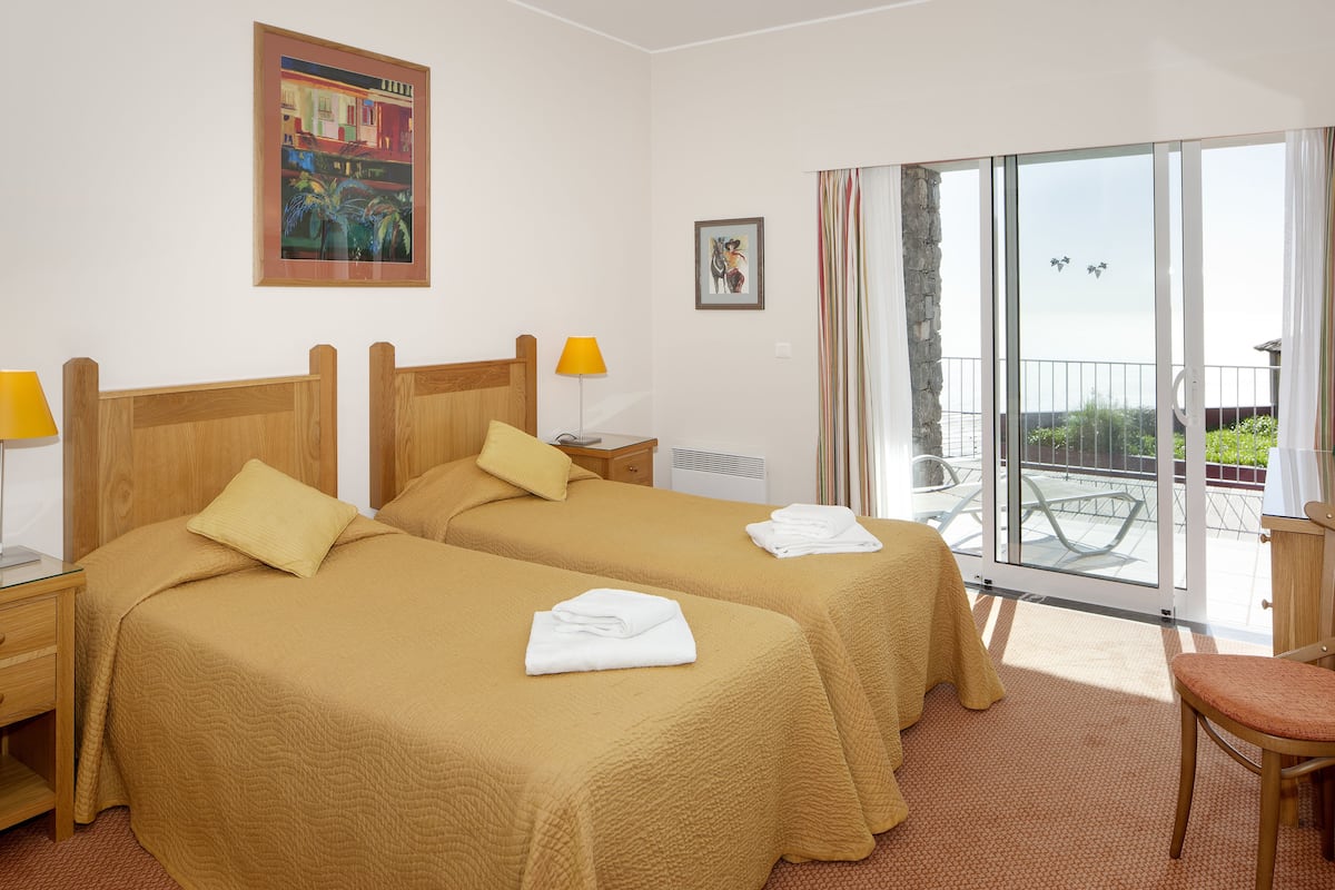 A hotel room with two beds, a balcony with a view, and a table with a chair.