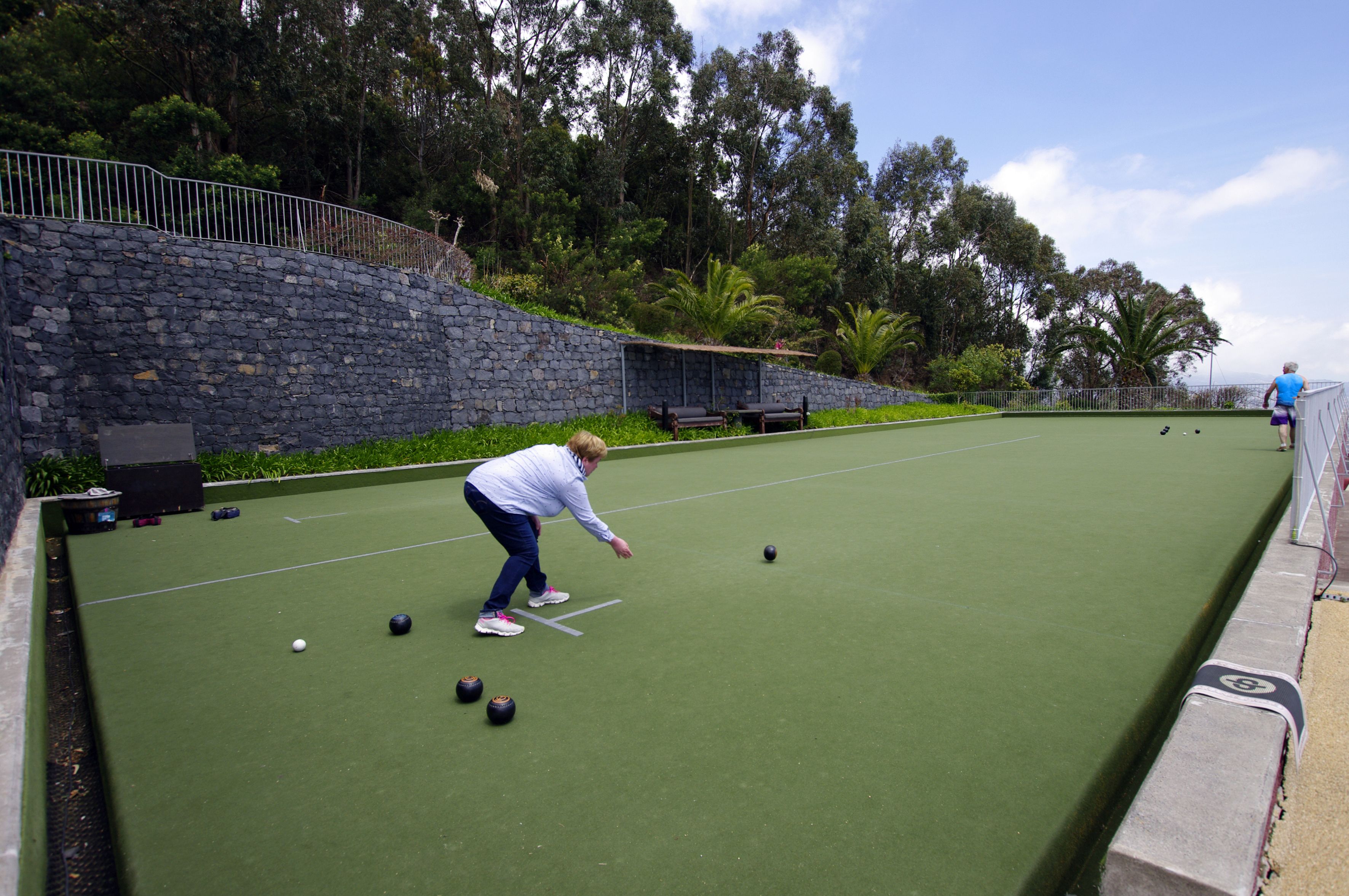 A croquet court with a stone wall and greenery in the background.
