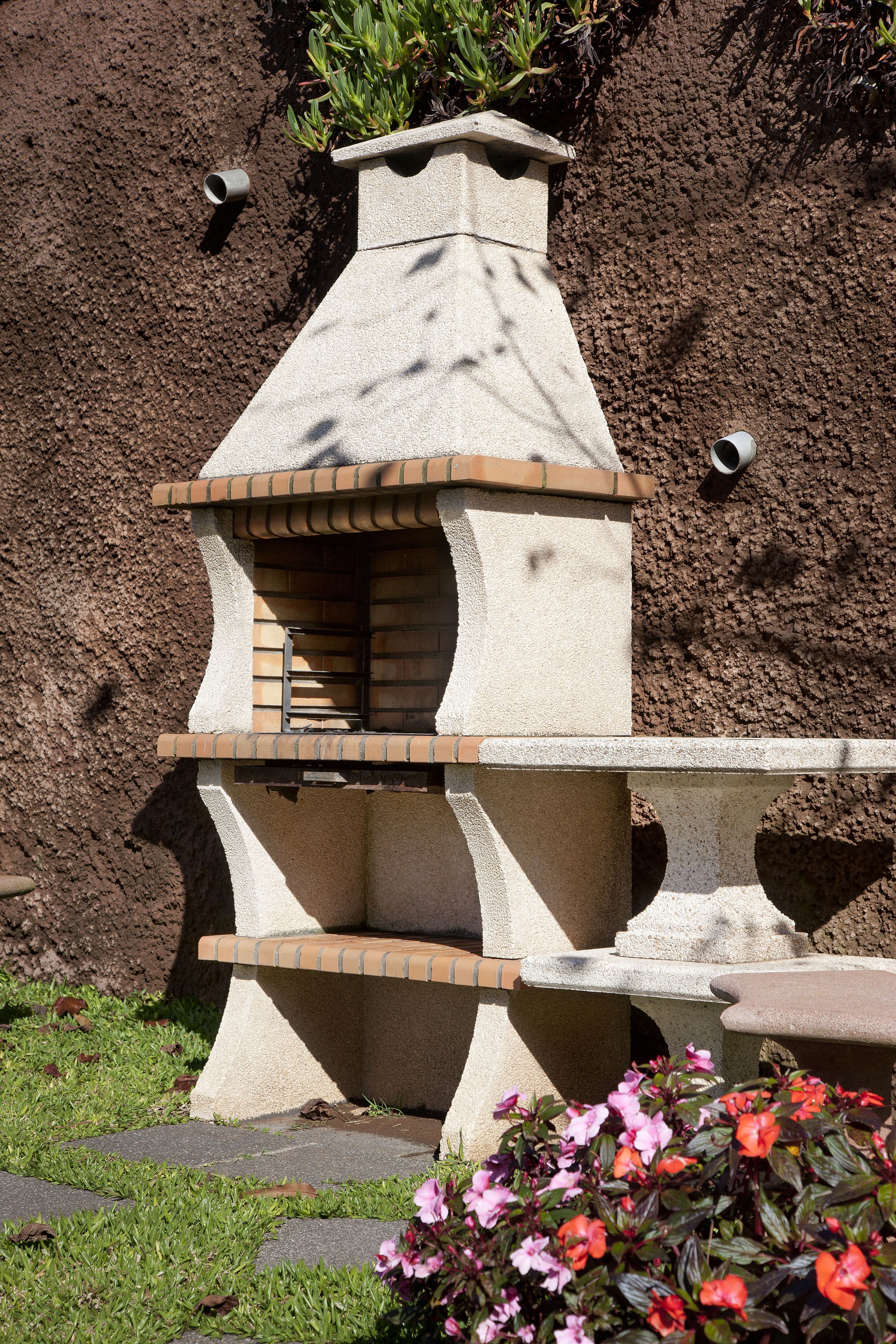 Un horno de piedra con interior de ladrillo, rodeado de césped y plantas en flor.