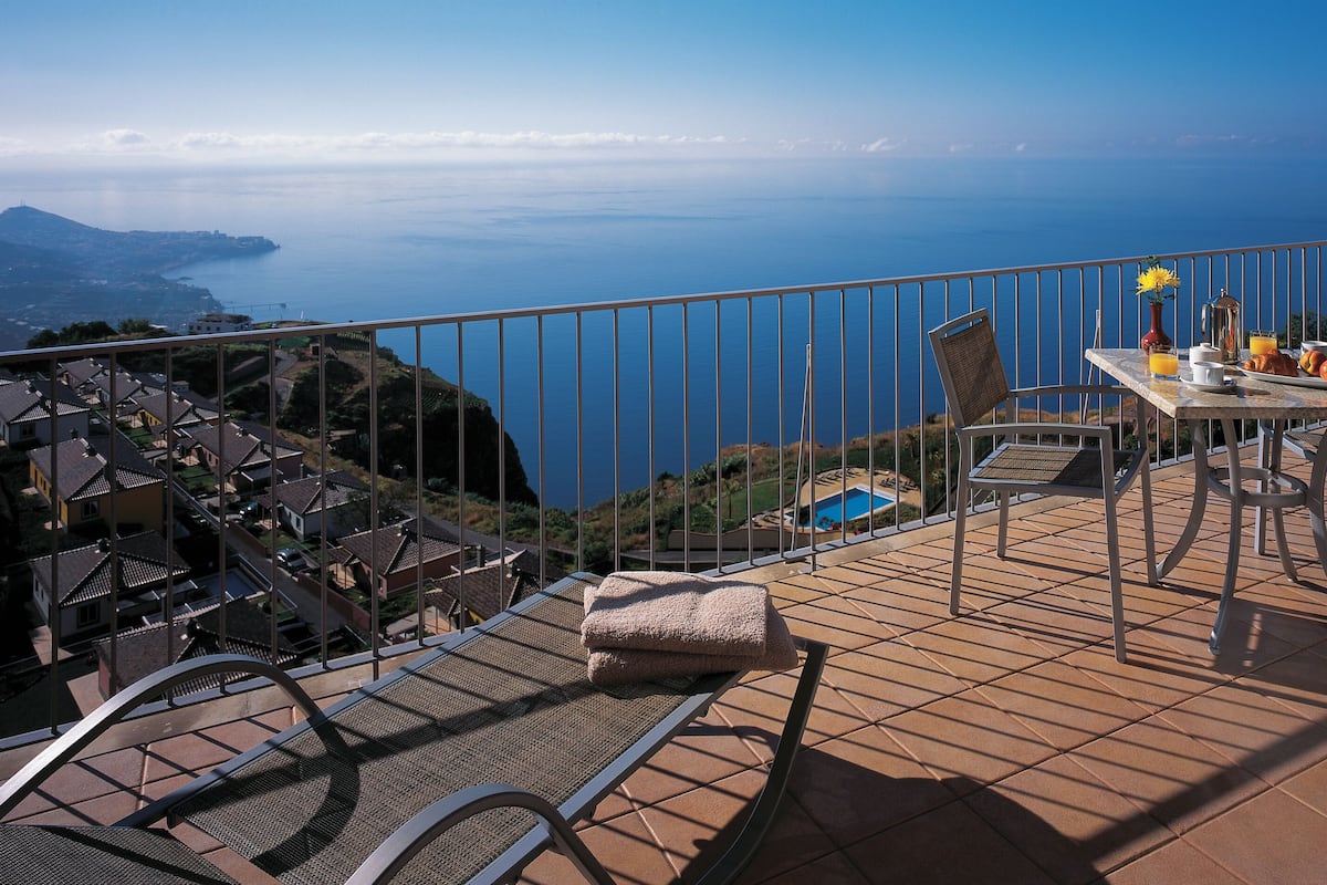 A terrace with a table set for breakfast, overlooking a coastal view.