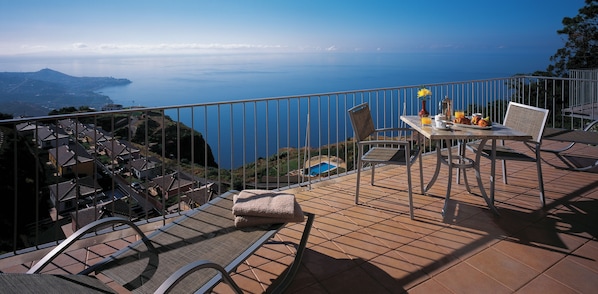 A terrace with a table set for breakfast, overlooking a coastal view.