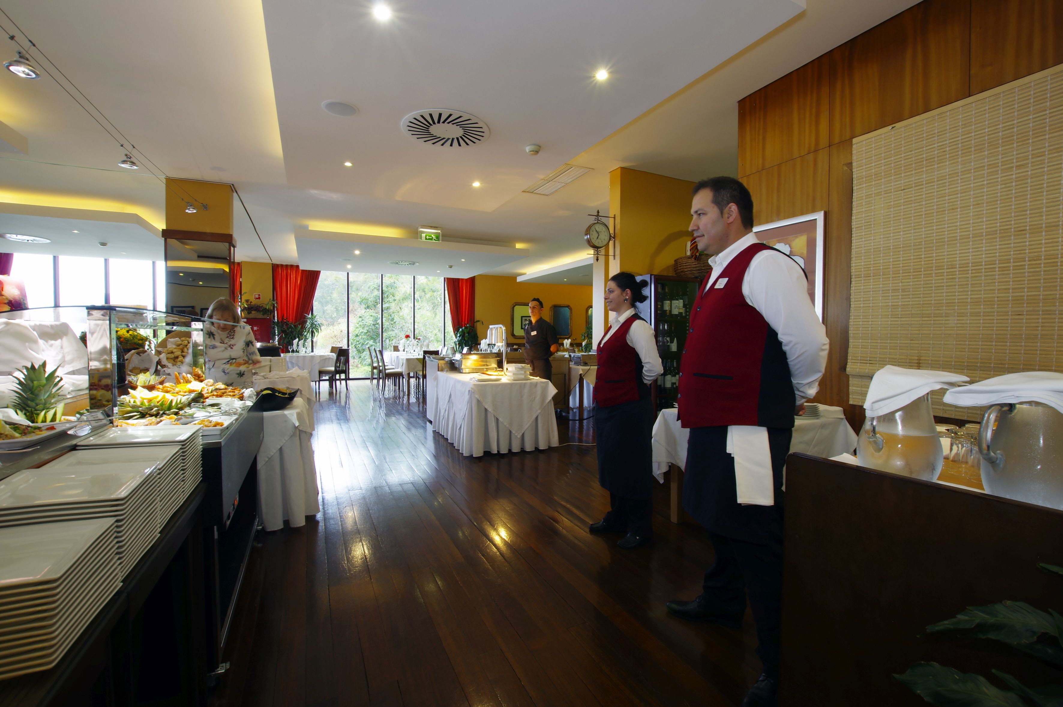 Une salle à manger d'hôtel avec des tables de buffet, du personnel en uniforme et une grande fenêtre en arrière-plan.