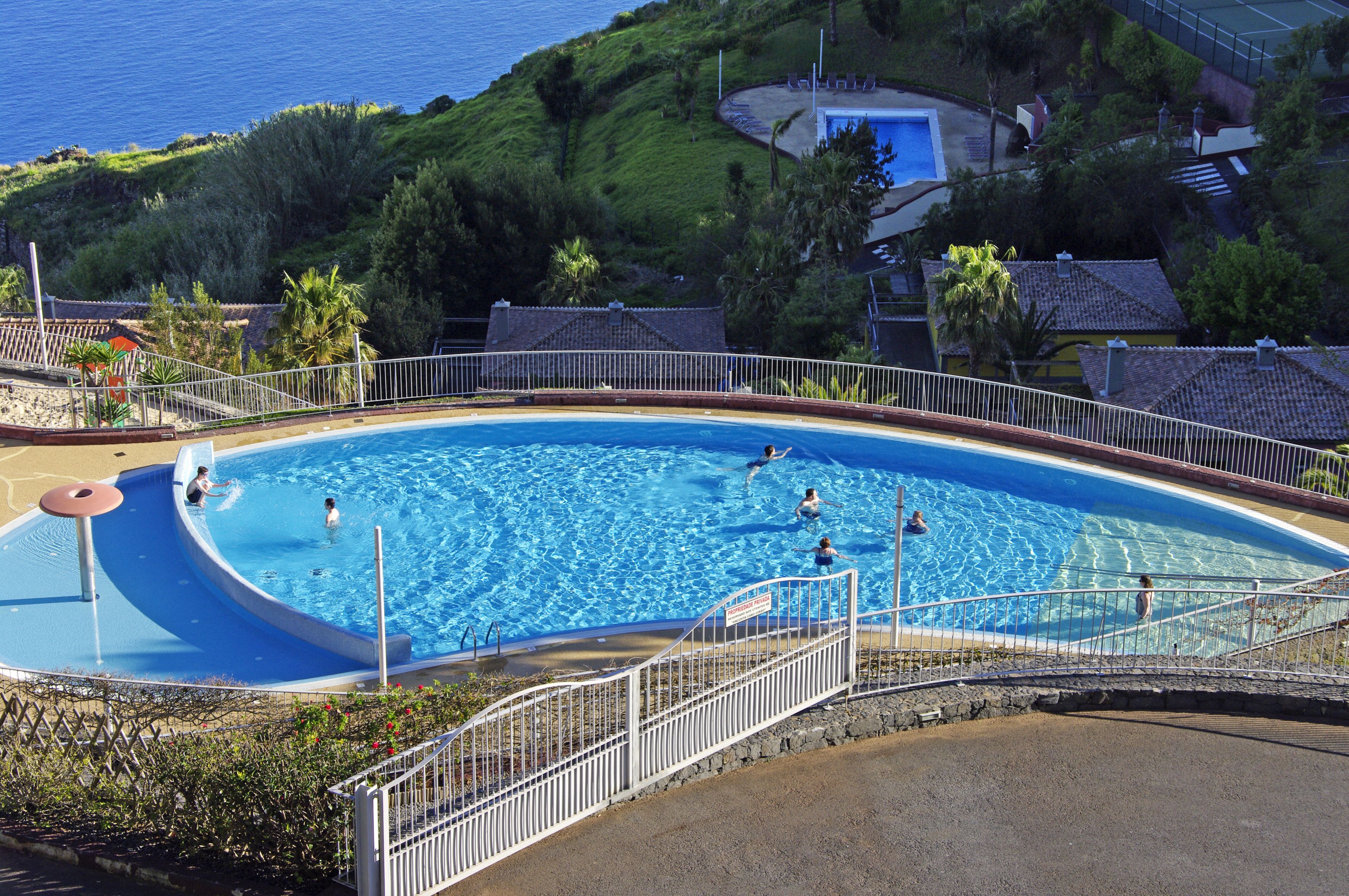 En swimmingpool med et bølgende design, omgivet af et hvidt hegn og en stenvæg.