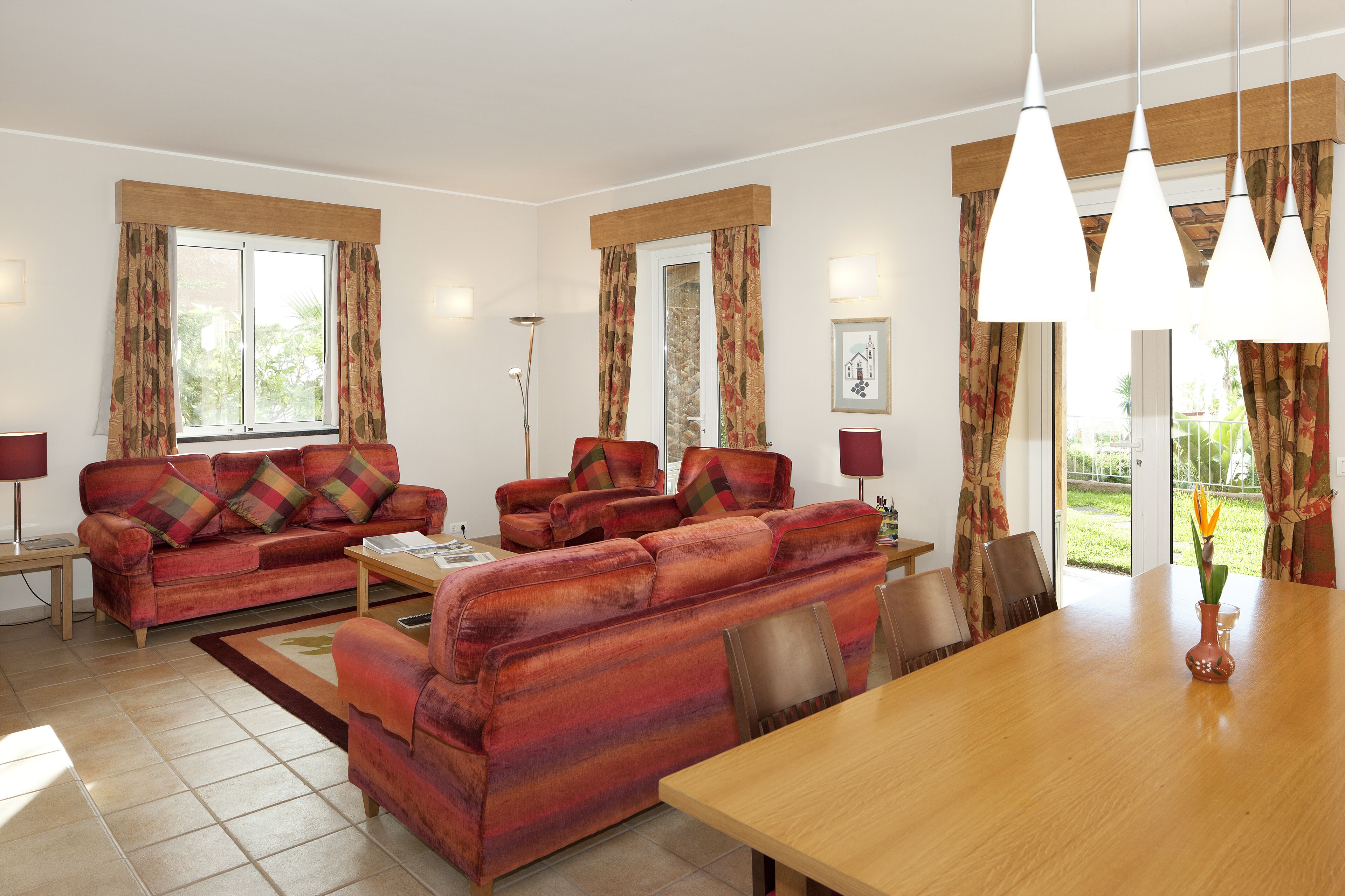 A living room with a sofa set, a dining table, and a vase with flowers.