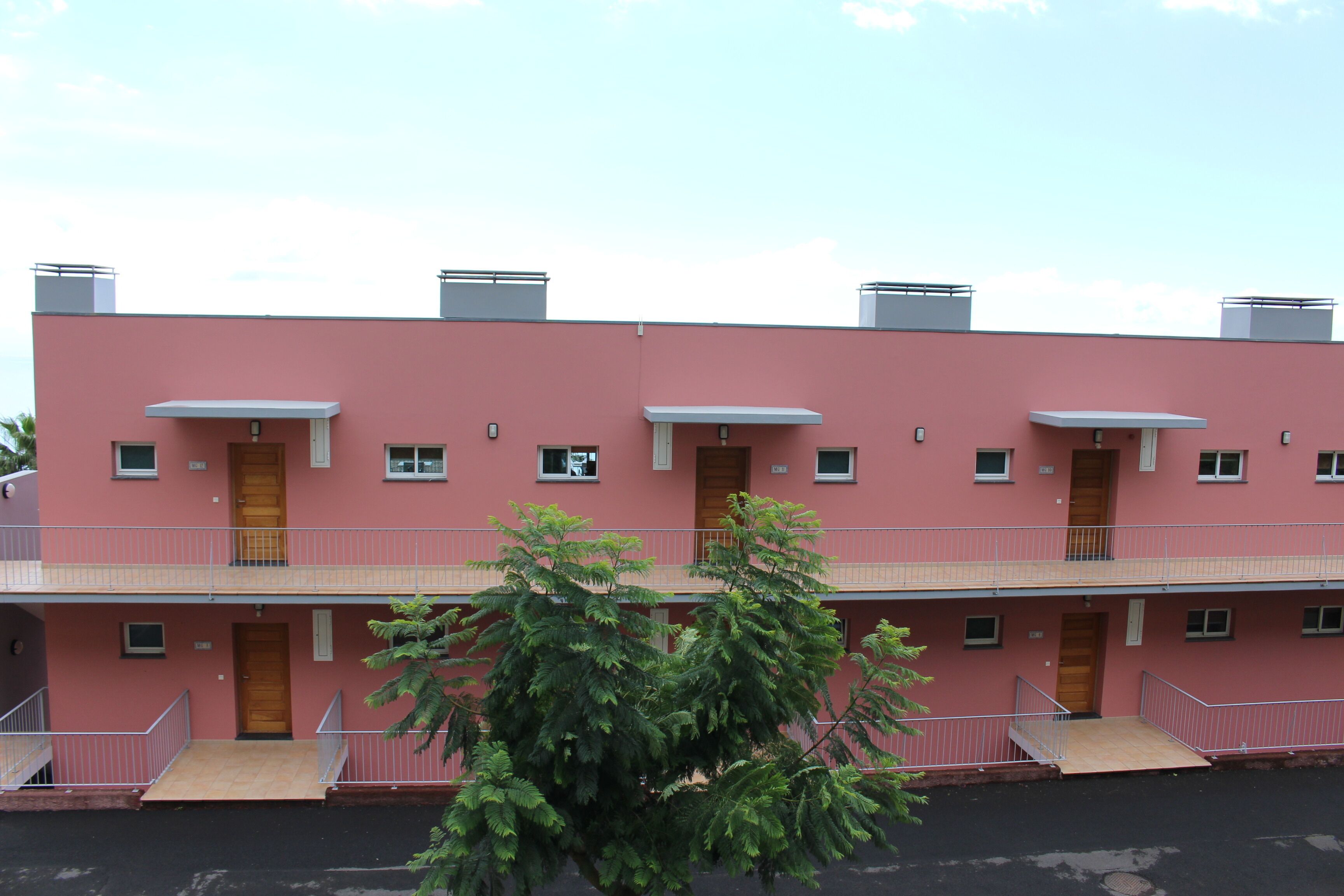 Ein pinkfarbenes Mehrfamilienhaus mit Balkonen, Holztüren und kleinen Fenstern.