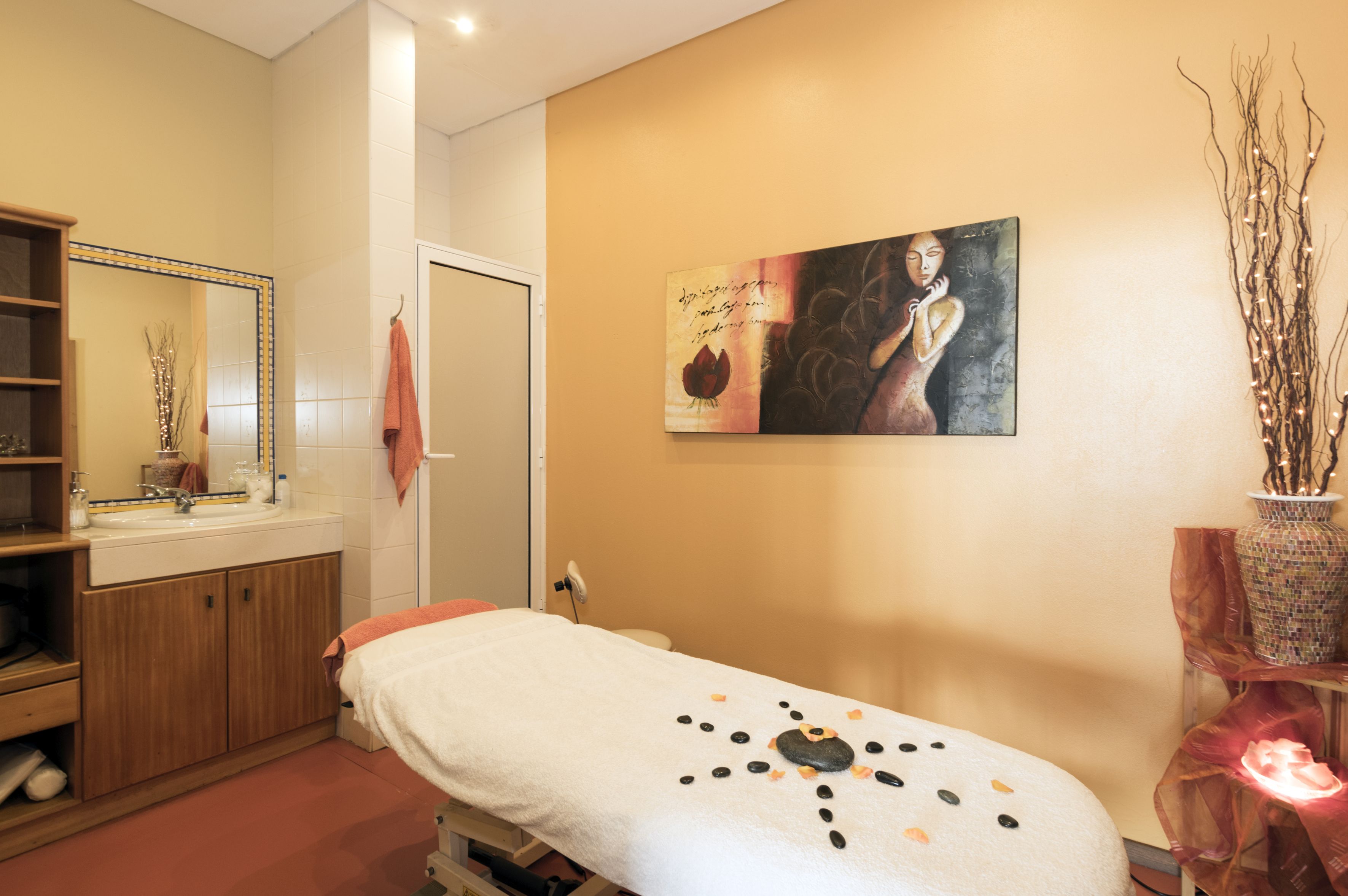A spa room with a massage table, a wooden cabinet, a mirror, and a painting on the wall.