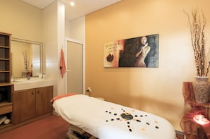 A spa room with a massage table, a wooden cabinet, a mirror, and a painting on the wall.