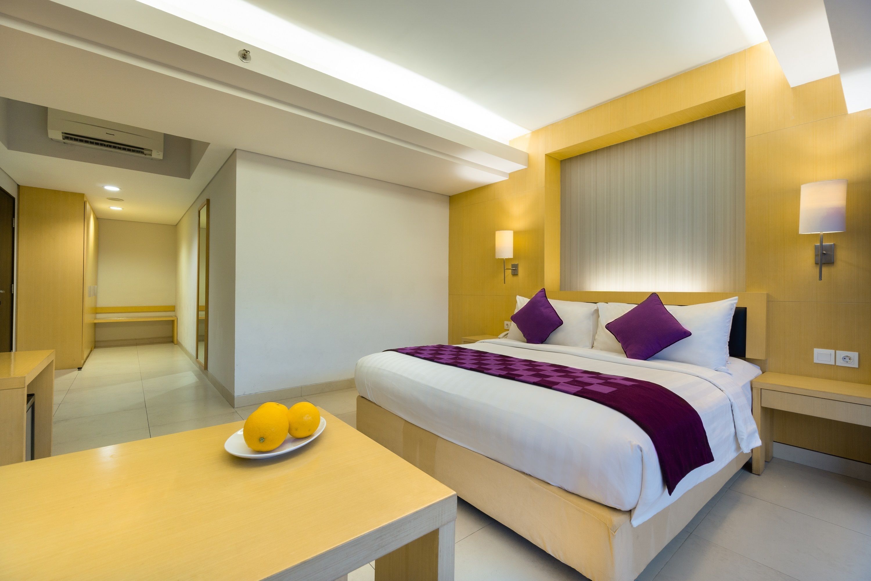 A modern hotel room with a large bed, bedside tables, a bedside lamp, and a fruit bowl on a table.
