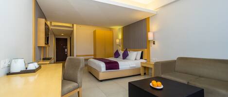 A hotel room with a bed, a sofa, a coffee table, a desk, and a chair.
