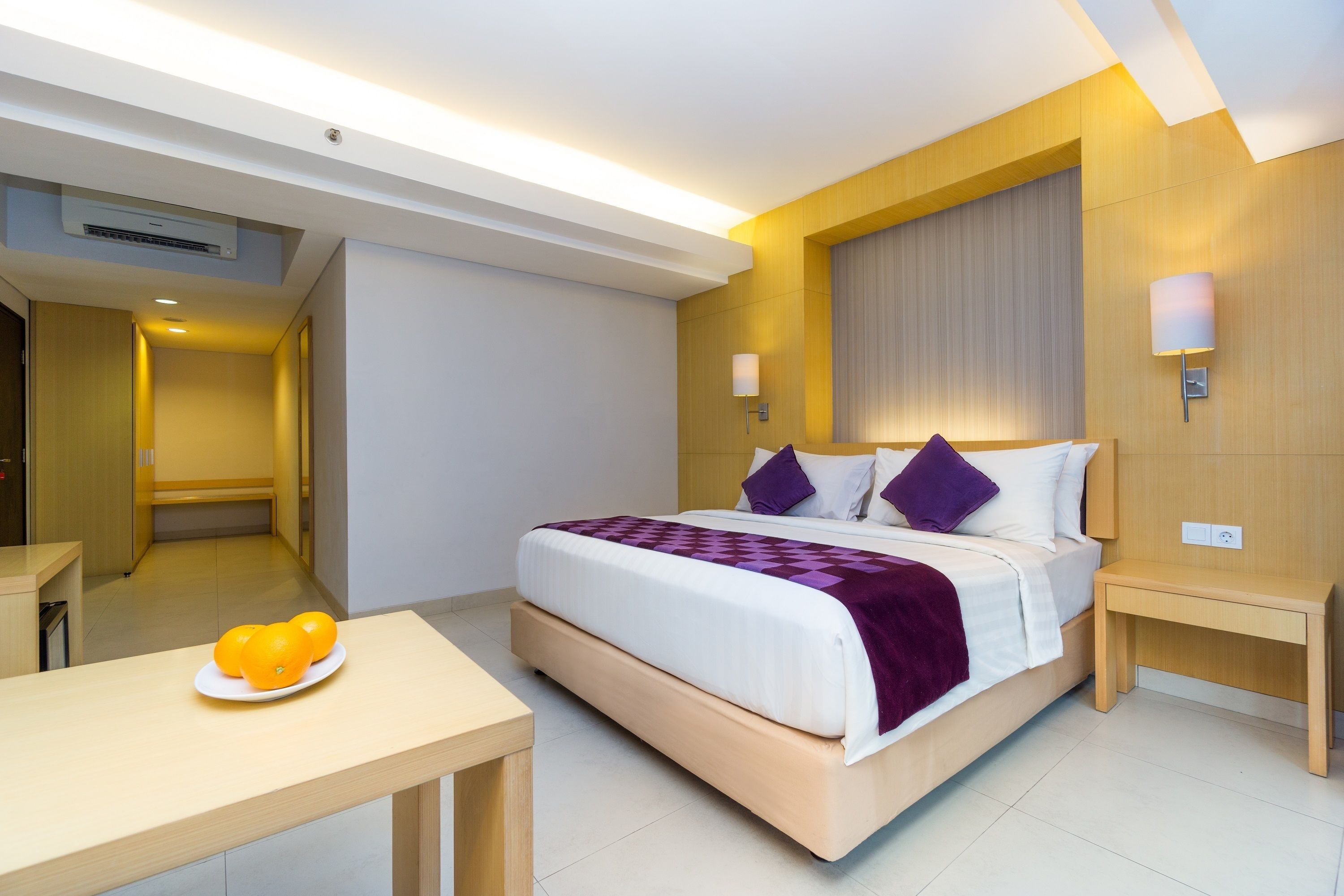 A modern hotel room with a large bed, bedside tables, a small desk, and a plate of oranges.