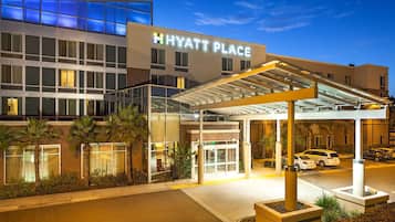 A Hyatt Place hotel entrance with a glass facade, palm trees, and a covered walkway.