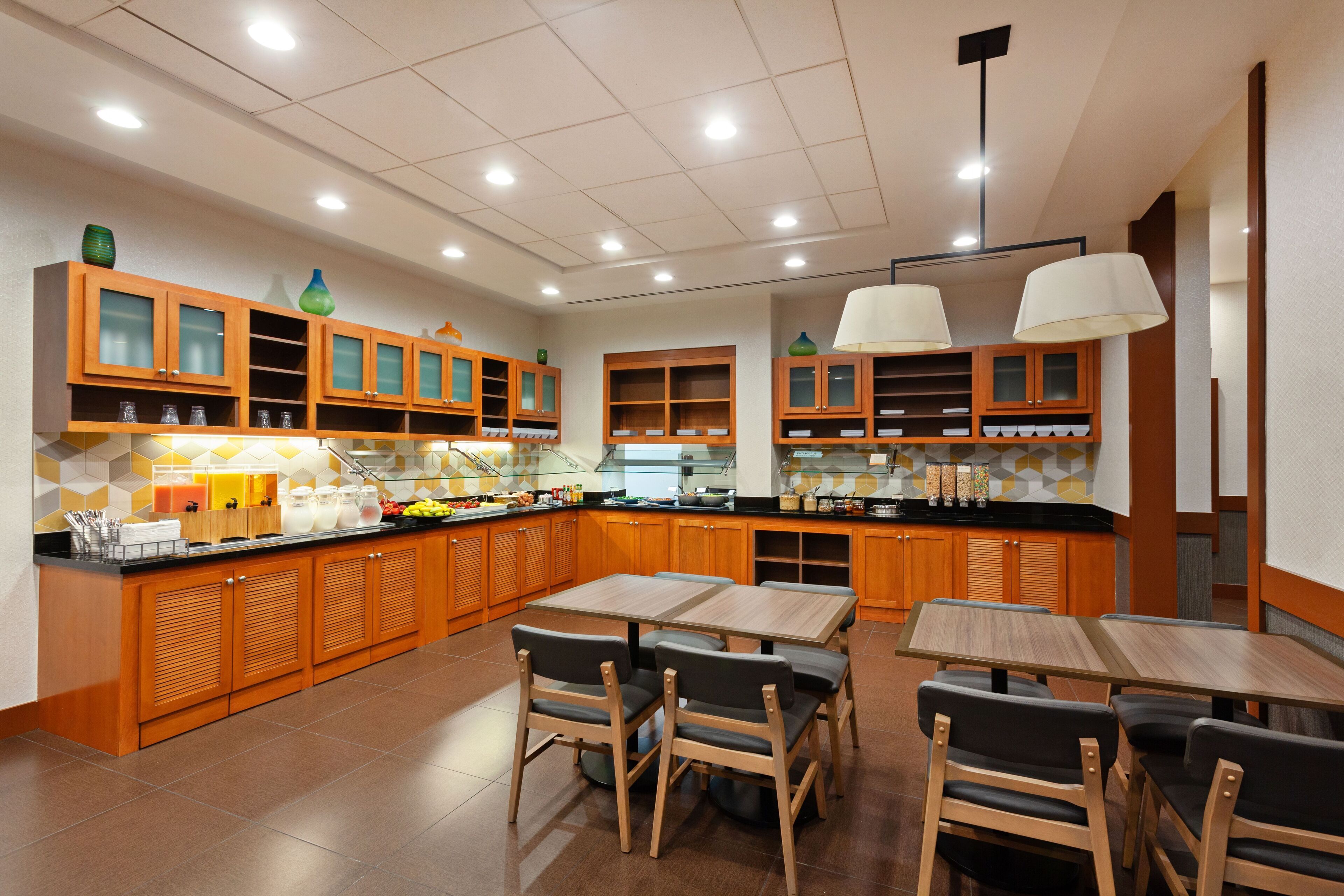 Una cocina moderna con armarios de madera, una isla central y un comedor con mesas y sillas.
