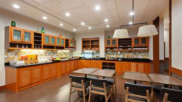 Una cocina moderna con armarios de madera, una isla central y un comedor con mesas y sillas.