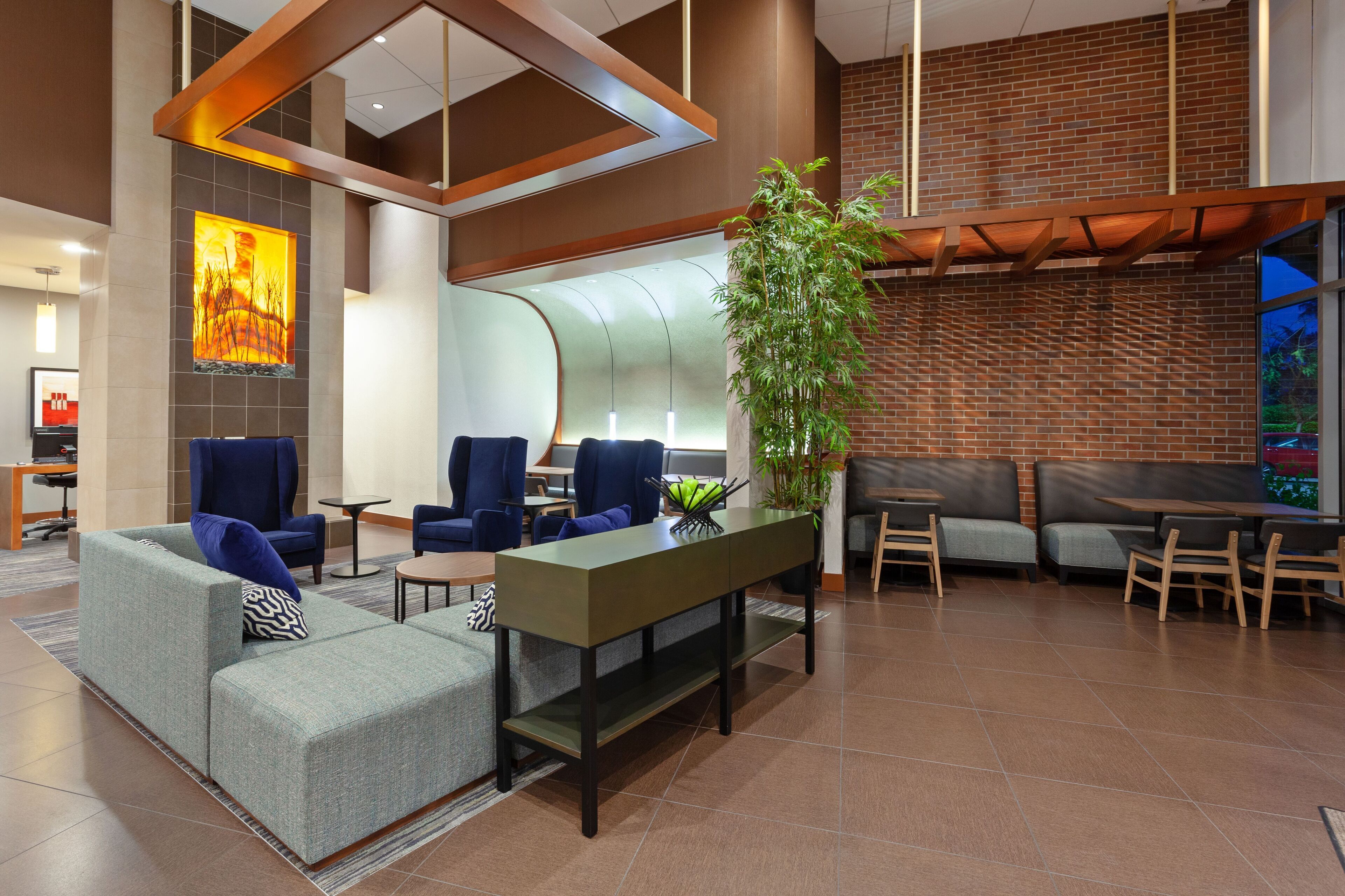 A modern lobby with seating areas, a large plant, and a brick wall.
