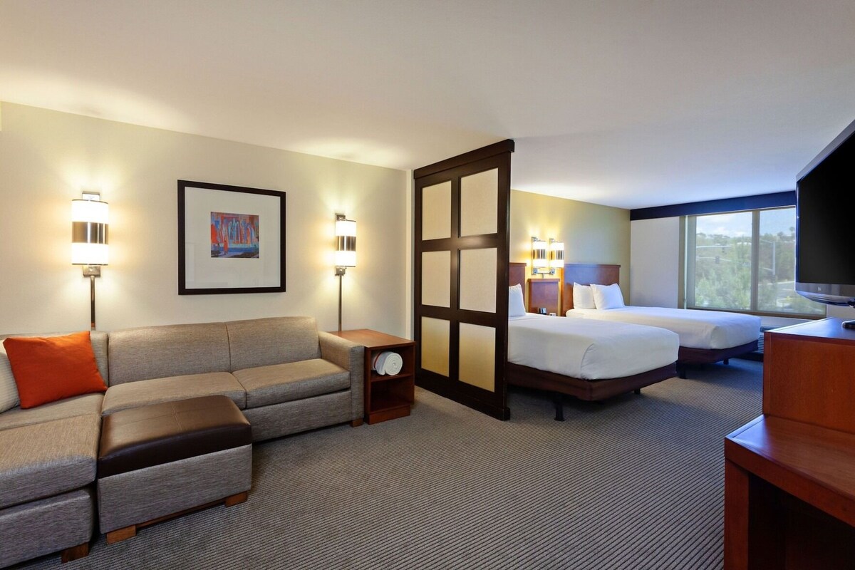 Habitación de hotel con sofá, dos camas, televisor y un cuadro en la pared.