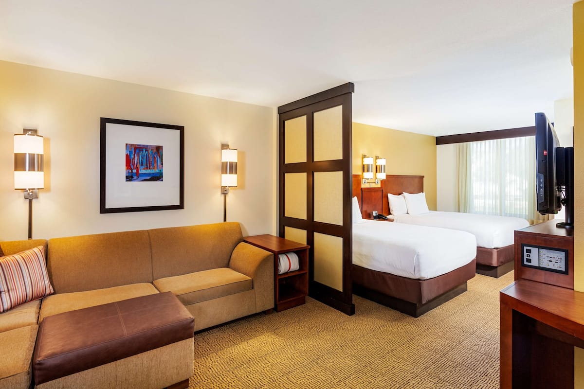 A hotel room with a sofa, two beds, a TV, and a framed picture on the wall.